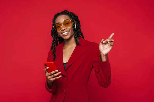 Black Young Woman Pointing Finger Aside Using Cellphone Isolated Red — Fotografia de Stock