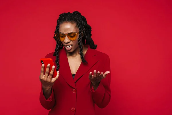 Black Young Woman Frowning Gesturing While Using Cellphone Isolated Red — Fotografia de Stock