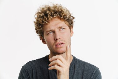 Kafası karışmış genç bir adam, çenesini tutup beyaz duvarın ötesine bakıyor.