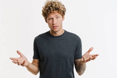 Kafası karışmış genç bir adam beyaz duvarın üzerinde izole bir şekilde kameraya bakıyor.