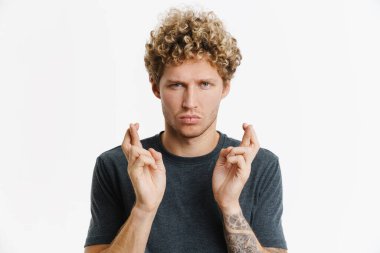 İyi şans için dua eden genç sarışın adam beyaz duvarda izole edilmiş.