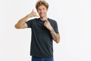 Genç sarışın adam işaret ediyor ve beyaz duvarın üzerinde izole edilmiş bir çağrı hareketi yapıyor.