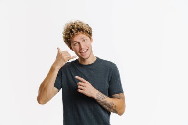 Genç sarışın adam işaret ediyor ve beyaz duvarın üzerinde izole edilmiş bir çağrı hareketi yapıyor.