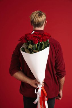 Sarışın sakallı adam kırmızı arka planda sakallı gül buketi ile poz veriyor.