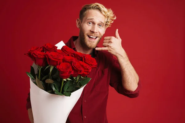 White bearded man making call gesture while posing with roses isolated over red wall