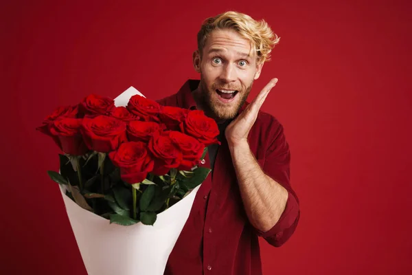 White bearded man expressing surprise while posing with roses isolated over red wall