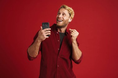 Sarışın, mutlu, müzik dinleyen kulaklıklı ve kırmızı duvarın üzerinde dans eden adam.