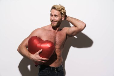 Beyaz arka planda izole edilmiş kalp balonuyla poz verirken gülümseyen üstsüz sarışın adam.