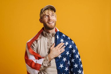 Beyaz bir asker göğsünde Amerikan bayrağı taşıyor. Sarı duvardan izole edilmiş.