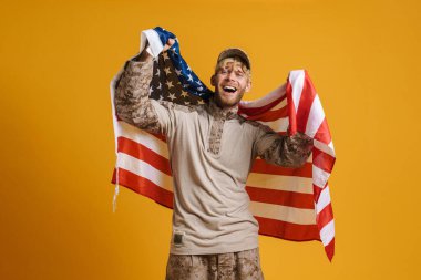White military man screaming while posing with american flag isolated over yellow wall