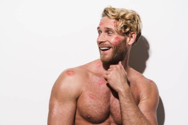 Beyaz tişörtsüz, ruj izi olan beyaz bir adam, gülümsüyor ve beyaz duvarın ötesine bakıyor.