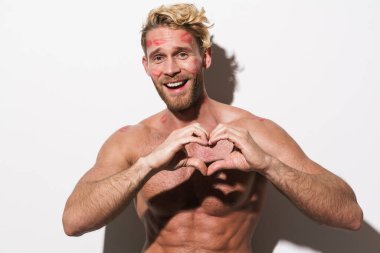 Ruj lekeli gömleksiz sarışın adam beyaz arka planda izole edilmiş kalp hareketi gösteriyor.