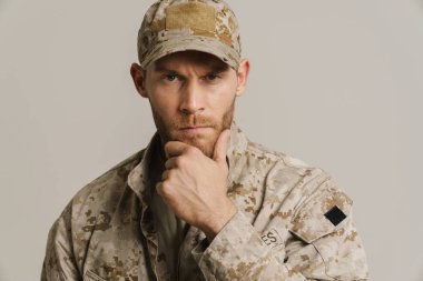 Beyaz asker çenesini tutuyor ve beyaz duvarın üzerinden izole edilmiş kameraya bakıyor.