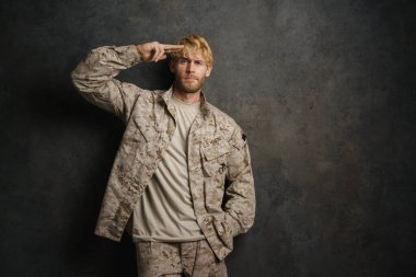 Beyaz asker üniformalı selam veriyor ve gri duvardan izole edilmiş kameraya bakıyor.