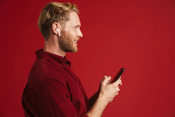 Blonde Man Listening Music Earphones Using Cellphone Isolated Red Wall — Stock fotografie