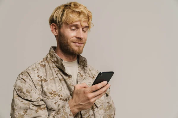 White military man wearing uniform smiling and using cellphone isolated over white wall