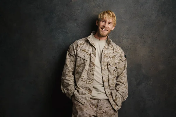 White military man wearing uniform smiling and looking at camera isolated over grey wall