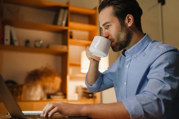 Mladý Štětinatý Muž Pití Kávy Při Práci Notebookem Kanceláři — Stock fotografie