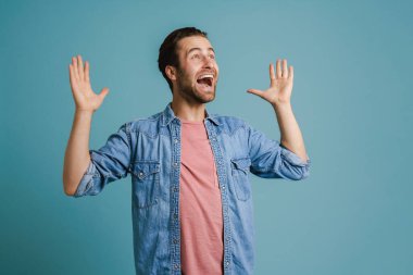 Mavi arka planda elleri havada, tişört giyen heyecanlı genç adam çığlık atıyor.