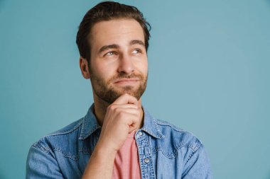 Kafası karışmış genç adam gülümsüyor ve mavi arka planda bir kenara bakıyor.