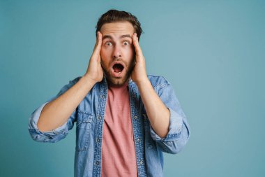 Young man holding his head while expressing surprise isolated over blue background