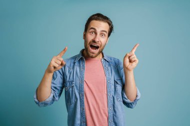 Genç kıllı adam, mavi arka planda mahsur kaldığını belirterek parmağını kenara kaldırarak sürpriz yapıyor.