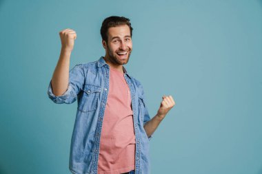 Heyecanlı genç adam çığlık atarak mavi arka planda izole edilmiş bir jest yapıyor.