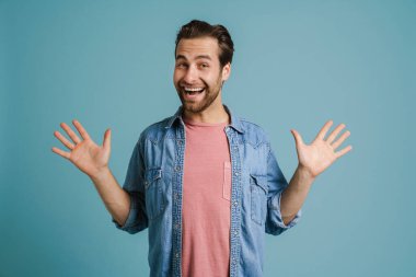 Young excited man smiling while showing his palms at camera isolated over blue background