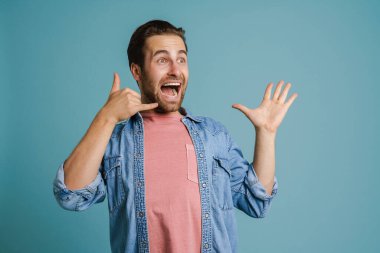 Heyecanlı genç adam mavi arka planda çığlıklar atıp el kol hareketi yapıyor.