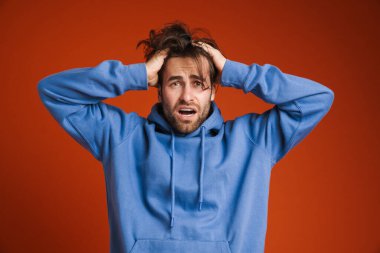 Young man holding his head while expressing surprise isolated over red background