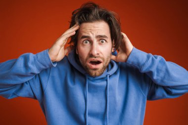Young man holding his head while expressing surprise isolated over red background