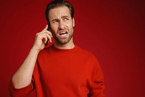 Young Bristle Man Frowning While Talking Cellphone Isolated Red Background — стоковое фото