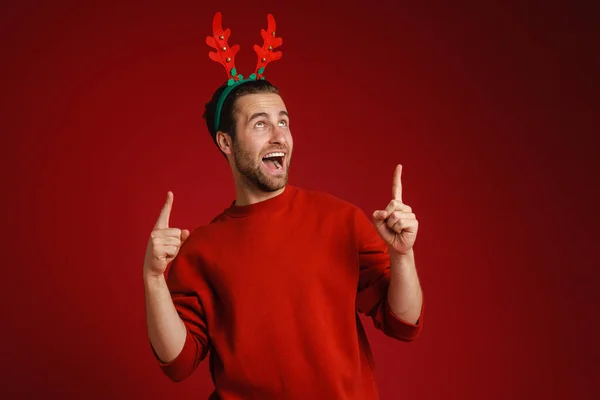 Young Man Wearing Christmas Antlers Pointing Fingers Upward Isolated Red — Foto Stock