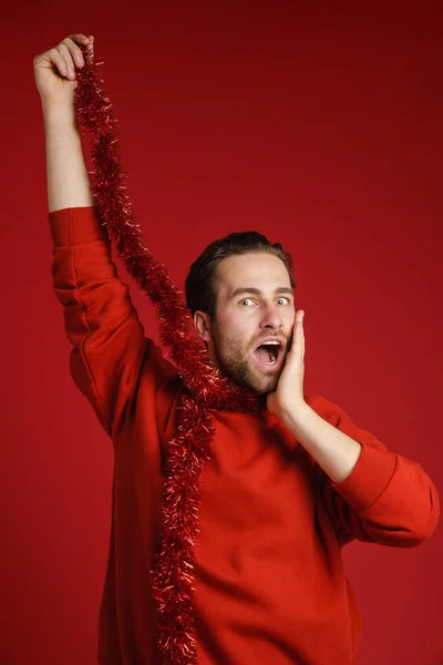 Young Bristle Man Expressing Surprise Making Fun Tinsel Isolated Red — Stockfoto