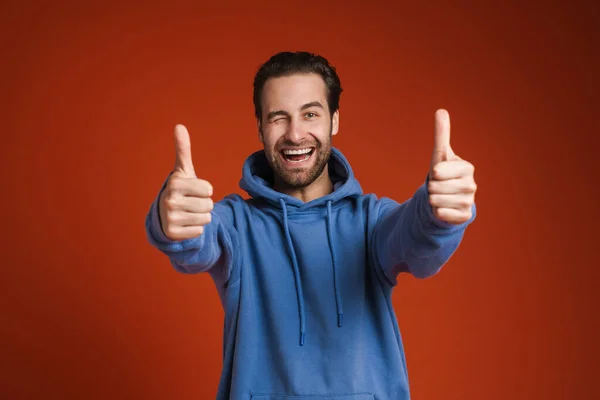 Young Bristle Man Winking Smiling While Showing Thumbs Isolated Red — Stockfoto