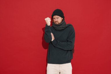 Beyaz adam, kırmızı arka planda izole edilmiş kameraya yumruk atarken kaşlarını çatıyor.