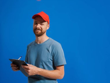 Mavi arka planda izole edilmiş, gülümseyen ve panoya yazı yazan beyaz kızıl adam.