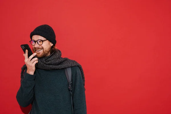 Імбирний Чоловік Капелюсі Шарфі Посміхається Використовує Мобільний Телефон Ізольовано Червоному — стокове фото
