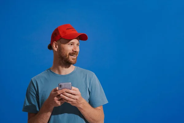 White Ginger Man Wearing Cap Smiling Using Cellphone Isolated Blue — 图库照片