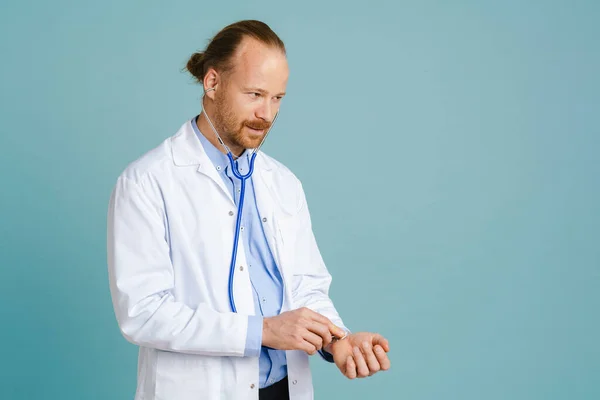 White male doctor wearing lab coat using stethoscope isolated over blue background