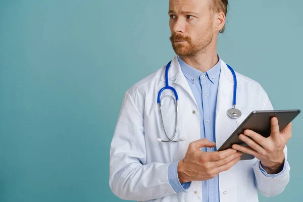 White male doctor wearing lab coat using tablet computer isolated over blue background