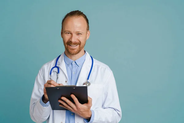 White Male Doctor Wearing Lab Coat Smiling While Writing Clipboard — Fotografia de Stock