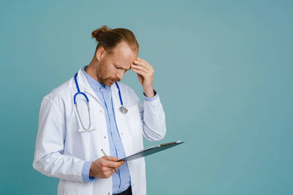 Puzzled Male Doctor Wearing Lab Coat Posing Clipboard Isolated Blue — стоковое фото