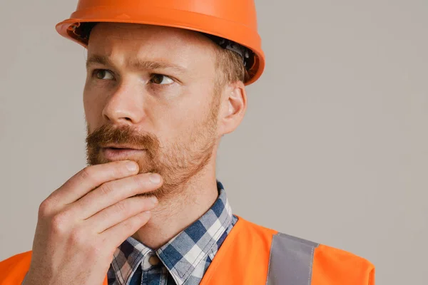 White man worker wearing helmet and vest looking aside isolated over grey background