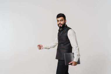 Sakallı Güney Asyalı adam beyaz duvarın üzerinde dizüstü bilgisayarla poz veriyor.