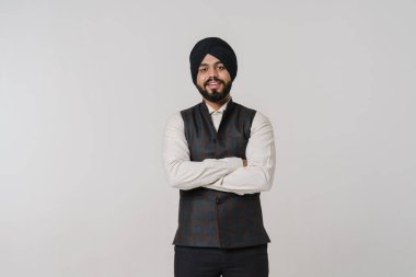 Sarıklı Güney Asyalı adam gülümsüyor ve beyaz duvarın üzerinden izole edilmiş kameraya bakıyor.