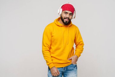 Sakallı Güney Asyalı adam, beyaz duvarda izole edilmiş kulaklıklarla müzik dinliyor.