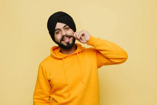Bearded south asian man wearing turban smiling at camera crossed isolated over yellow wall