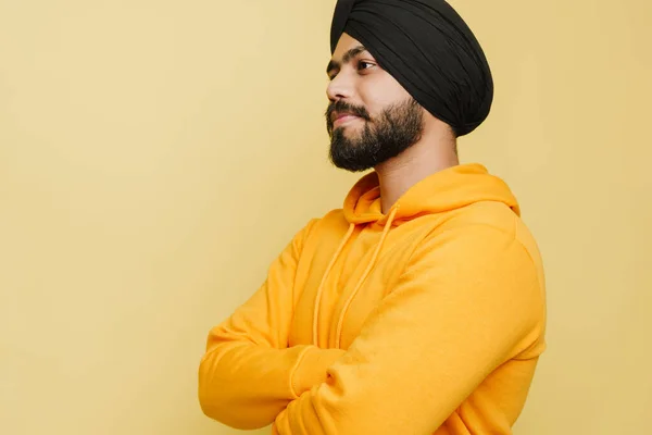 Bearded south asian man wearing turban posing with arms crossed isolated over yellow wall