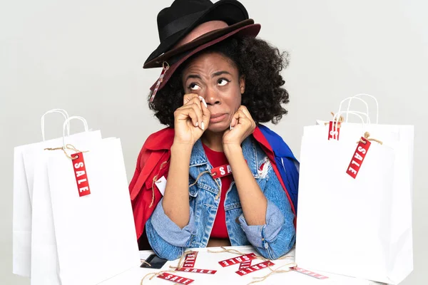 Black young woman crying while posing with shopping bags isolated over white background